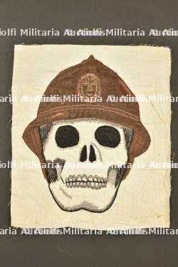 Broderie representant un crane coiffe d’un casque Adrian belge. Embroidery depicting a skull wearing a Belgian Adrian helmet.